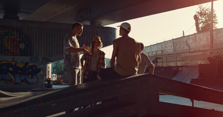 Stylish millennials relaxing skatepark. Hipsters talking together at sunset.