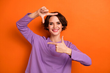 Wall Mural - Portrait of positive pretty person arms fingers demonstrate cadre isolated on orange color background