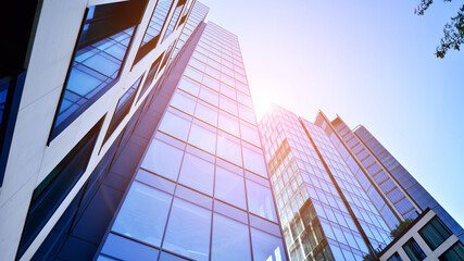 Wall Mural - Bottom view of modern skyscraper in business district against blue sky. Looking up at business buildings in downtown. Rising sun on the horizon.