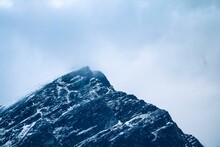 Closeup Of A Rocky Mountain Peak Covered With Snow On A Cloudy Day