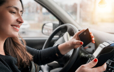 young latin woman in a car paying with card at gas station or business