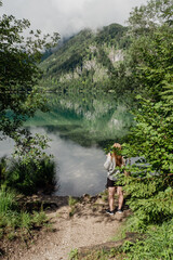 Wall Mural - young woman behind the trees looking at the crystal clear water reflection of a lake in the mountains