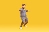 Fototapeta  - Plus size male model in funny PJs having fun in modern fashion studio. Happy carefree confident fat bearded man in comfortable leopard pajamas and cool glasses dancing isolated on yellow background