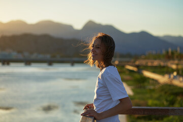 Portrait of a beautiful young woman enjoying nature with mountains and sunset sky, relaxing at landscape