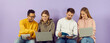 © Studio Romantic - Happy multiracial college or university students sitting in row by purple wall, using laptop computer devices, preparing for class, helping each other, doing group project, sharing course study notes