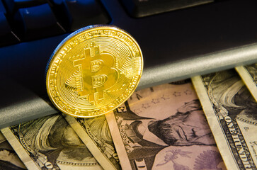 Golden coin of bitcoin and dollars banknotes near computer keyboard