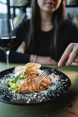 woman eat caesar salad with grilled chicken, romaine and crouton on black plate