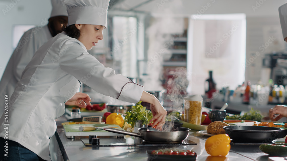 Female cook making professional culinary dish in frying pan, using food ...
