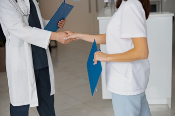 Wall Mural - Close up of two doctors in uniform shaking hands standing in clinic hall near reception