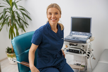 Wall Mural - Smiling doctor, ultrasound specialist looking at camera on her workplace in clinic