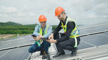 Engineer And Construction Worker Examining Solar Panels On Rooftop.
