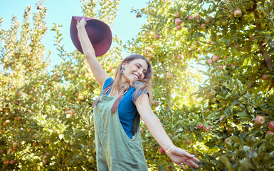 Wall Mural - Excited young woman jumping for joy in an apple orchard on a sunny day outside. Happy and cheerful farmer feeling optimistic, free and full of energy after a fruitful harvest on her successful farm
