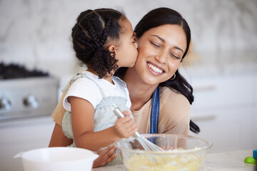 Canvas Print - Happy latin mother and daughter baking and sharing a kiss while bonding. A young woman helping her daughter bake or cook while stirring the batter and giving an affectionate hug in the kitchen