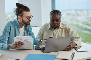 A young teacher explaining to senior student how do computer programming on a laptop.