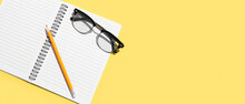 Pencil And Eyeglasses With Notebook On Yellow Background With Space For Text