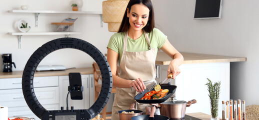 Wall Mural - Young female blogger recording video while cooking in kitchen