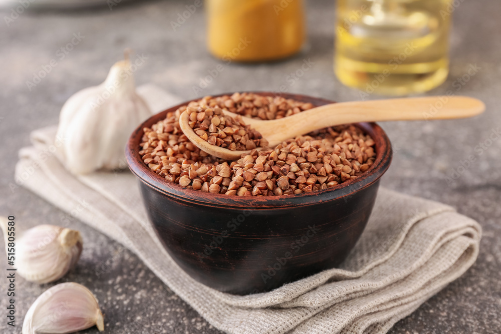 Bowl with buckwheat grains and garlic on grey table