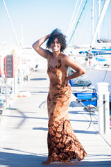 Wall Mural - Portrait of black young woman in elegant dress in tourist outdoor leisure activity. Ethnic beauiful girl enjoy sun and vacation at the harbour with blue sky in background