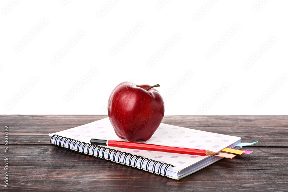 Notebook with pencil and apple on wooden table against white background