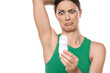 a horrified young woman applies deodorant under her armpits on a white background
