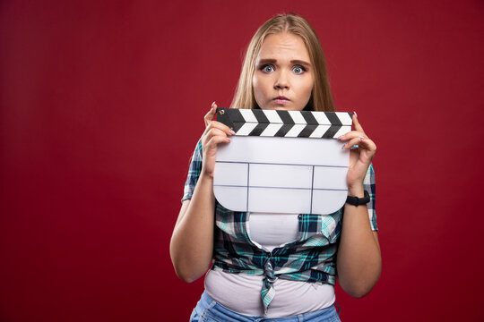 Young blonde model holding a blank movie filming clapper board and looks stressed and unexperienced