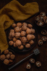 Wall Mural - Unpeeled walnuts on a ceramic plate with nut opener and yellow napkin on a dark wooden background.