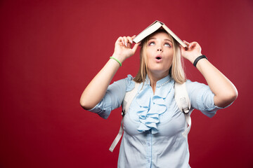 Wall Mural - Young blonde schoolgirl holds her book at her head and looks tired and confused