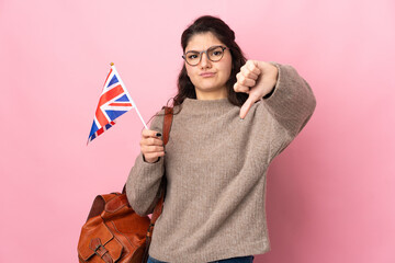 Wall Mural - Young Russian woman holding an United Kingdom flag isolated on pink background showing thumb down with negative expression