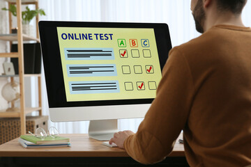 Man taking online test on computer at desk indoors, closeup