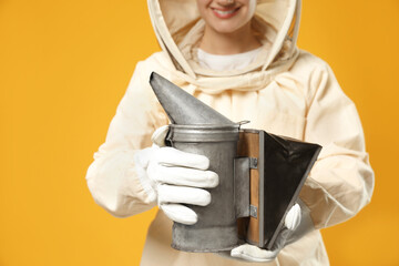 Beekeeper in uniform holding smokepot on yellow background, closeup