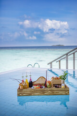 Breakfast in swimming pool, floating breakfast in luxurious tropical resort. Table relaxing on calm pool water, healthy breakfast and fruit plate by resort pool. Tropical couple beach luxury lifestyle