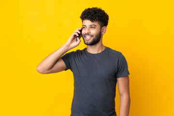 Young Moroccan man isolated on yellow background keeping a conversation with the mobile phone