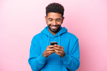 young brazilian man isolated on pink background sending a message or email with the mobile
