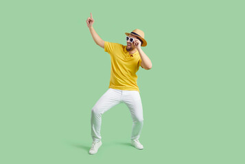 Funny man in summer hat and sunglasses isolated on green studio background dancing. Overjoyed happy guy enjoy summertime vacation or holiday, make dancer moves. Entertainment concept.