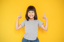Portrait Of Young Fun Smart Happy Little Cute Asian Girl Isolated On Yellow With Copy Space Studio Shot. Education For Elementary Kindergarten, Little Girl Finger Point Up Back To School Concept