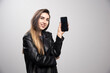 © rastockinc - Girl in leather jacket holding smart phone on a gray background