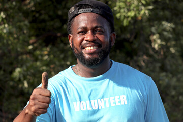 Happy smiling African volunteer man in blue t-shirt cleaning giving thumb up at mangrove forest, prepare to plant tree in deep mud for increasing mangrove cover world-wide, Eco world environment day.