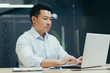© Liubomir - Serious and confident asian boss working in modern office, businessman typing on laptop.