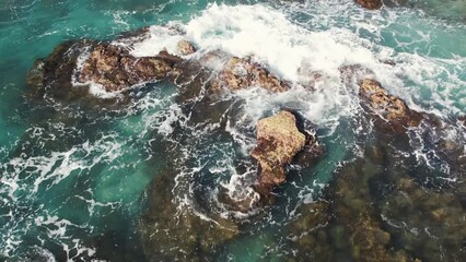 Poster - 4K aerial shot from a drone from above, the purest turquoise waters break on the rocks near the shore and foam. Surf splashes are scattered in slow motion
