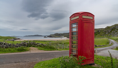 Poster - typical red English phone booth in the middle of nowhere next to a picturesque beach in Scotland with a coastal road