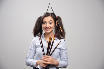 Wall Mural - Young woman artist with bunch of paintbrushes on gray background