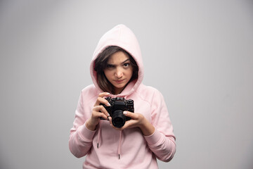 Wall Mural - Young woman in sweatshirt holding camera and looking at angrily