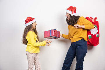 Wall Mural - Woman giving a present to young girl in Santa Claus red hat