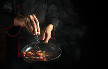 Professional Chef Adds Salt To A Steaming Hot Pan. The Idea Of European Cuisine For A Hotel With Advertising Space