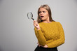 Blonde girl holds a magnifier and looking to it in a doubtful manner