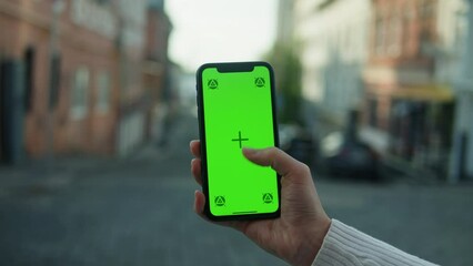 Woman holding smartphone with chroma key close-up. Young female person using phone with green screen outdoor.