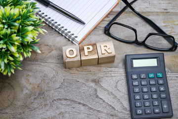 View from above of OPR wordings on the wooden blocks with a calculator, eyeglasses, and a pen on the notebook. Business and banking concept
