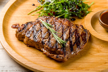 Poster - juicy Ribeye steak on wooden plate with aragula, tomatoes and pepper sauce macro close up