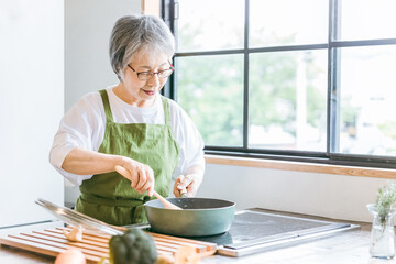 キッチンでフライパンを使うシニア女性
