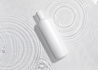 White cosmetic bottle on the water surface. Blank label for branding mock-up. Summer water pool fresh concept. Flat lay, top view.	